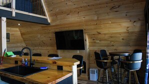 Een houten interieur met een keukenhoek, barstoelen en een flatscreen televisie aan de muur.
