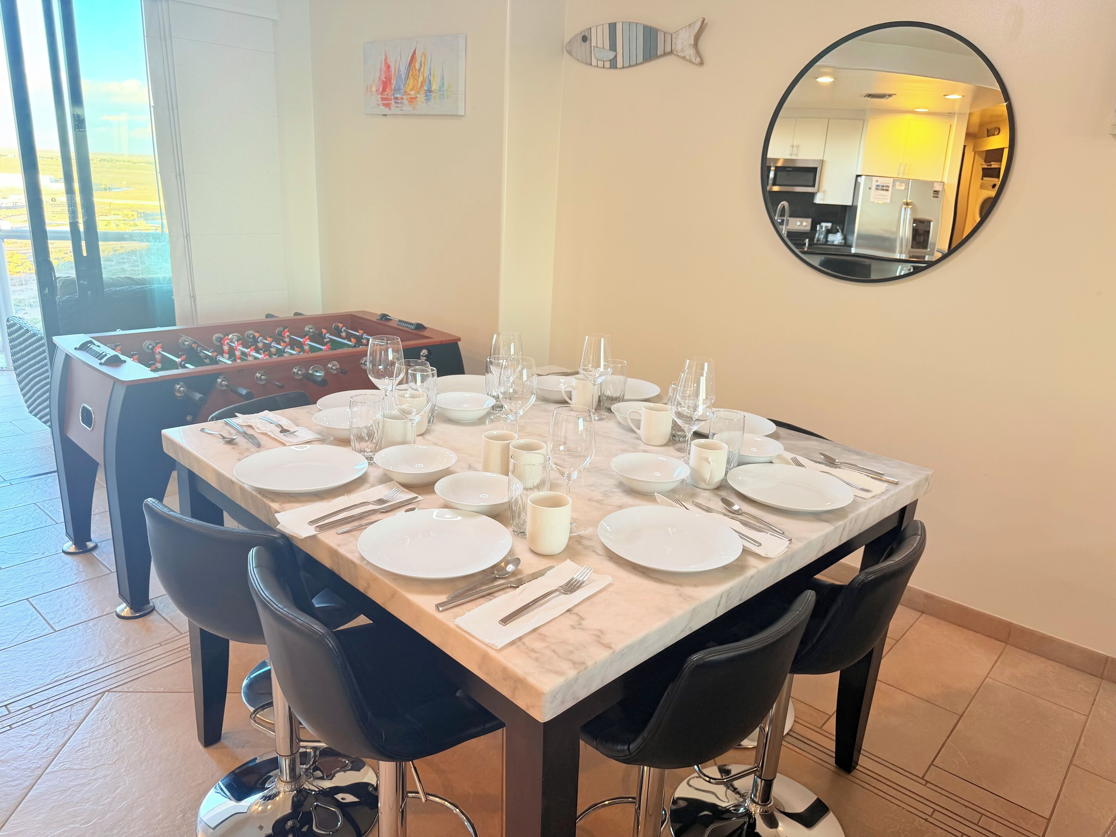 Un coin repas avec un baby-foot, un grand miroir rond et une vue sur la cuisine.