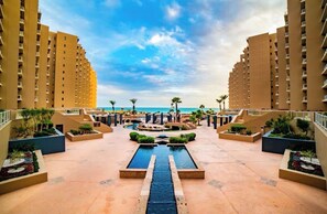 A resort with a central pool, palm trees, and a view of the ocean. - Las Palomas 4BR 4BA Suite 901 Cortez (Puerto Peñasco)