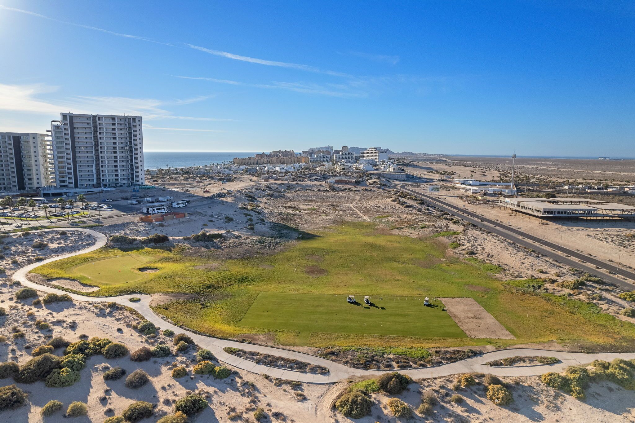 An aerial view of a coastal area with a golf course, buildings, and a road network.