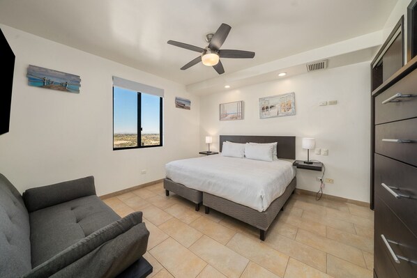 A bedroom with a bed, a ceiling fan, a nightstand, a lamp, a dresser, and a window with a view. - Las Palomas 4BR 4BA Suite 901 Cortez (Puerto Peñasco)