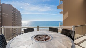 A round table with a fire pit in the center, surrounded by wicker chairs, overlooking a beach and ocean. - Las Palomas 4BR 4BA Suite 901 Cortez (Puerto Peñasco)