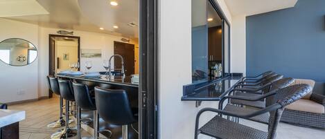 A modern kitchen with a bar area, bar stools, and a dining table.