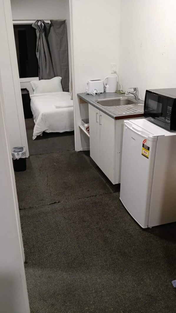 Habitación de hotel pequeña con kitchenette que incluye microondas, tostadora y lavamanos.