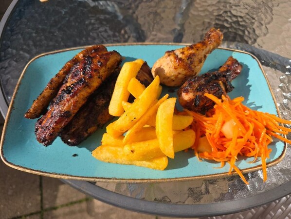 Un plato con alitas de pollo a la parrilla, papas fritas y zanahorias ralladas.