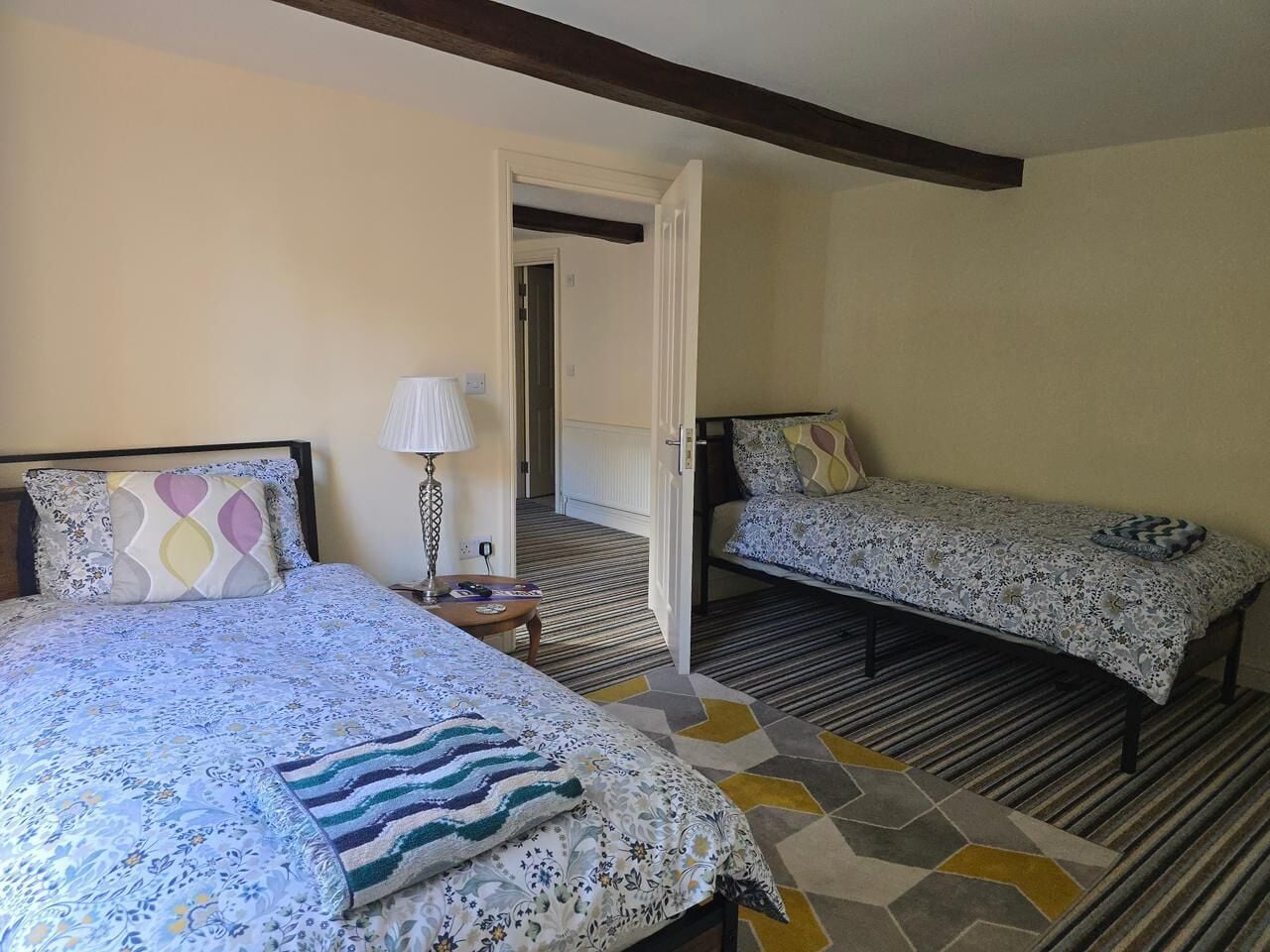A bedroom with two beds, a nightstand, and a door leading to another room.