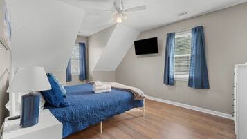 A bedroom with a bed, a ceiling fan, a TV mounted on the wall, and a window with curtains.