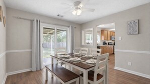 A dining area with a table set for four, white chairs, and a ceiling fan. - Home in Pooler w/ FirePit and Game Room (Pooler)