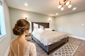 Une chambre à coucher avec une tête de lit capitonnée, un lit recouvert de linge de lit blanc, un tapis à motifs et une table de chevet avec une lampe.