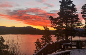 A lakeside view with a wooden deck overlooking the water, surrounded by trees and mountains in the background. - Pet friendly home in øydegard with house a panoramic view (Øydegard)