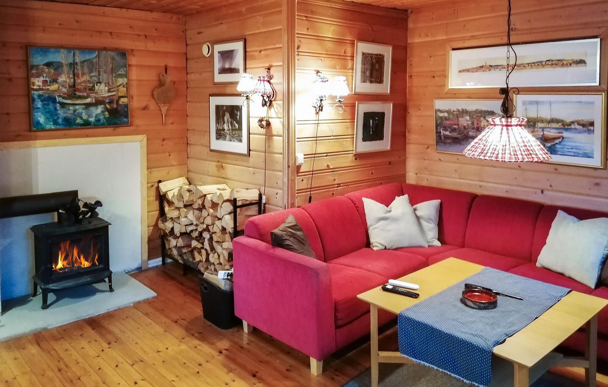 Interior acogedor de una cabaña con un sofá rojo, chimenea, paredes de madera y fotografías enmarcadas.
