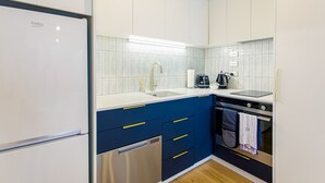 Una cocina moderna con armarios blancos, encimera azul y electrodomésticos de acero inoxidable, incluyendo un refrigerador, lavavajillas y horno.