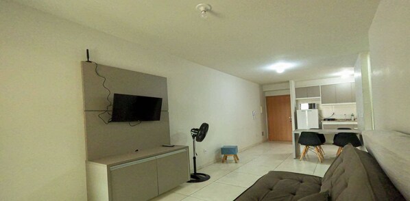 A living room with a flat-screen TV mounted on the wall, a sofa, a coffee table, and a dining area with a table and chairs.