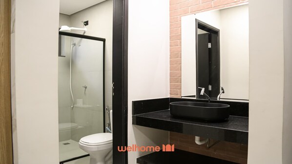 A modern bathroom with a glass-enclosed shower, a white toilet, and a black sink with a mirror above it. - Studio em Bauru com Boa Localização Perto da USP (Bauru)