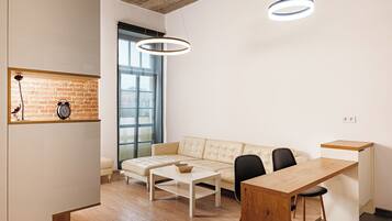 Un espacio habitable moderno con un sofá, una mesa de centro, una mesa de comedor y dos sillas. Se aprecia una pared de ladrillo y un ventanal grande que proporciona luz natural.