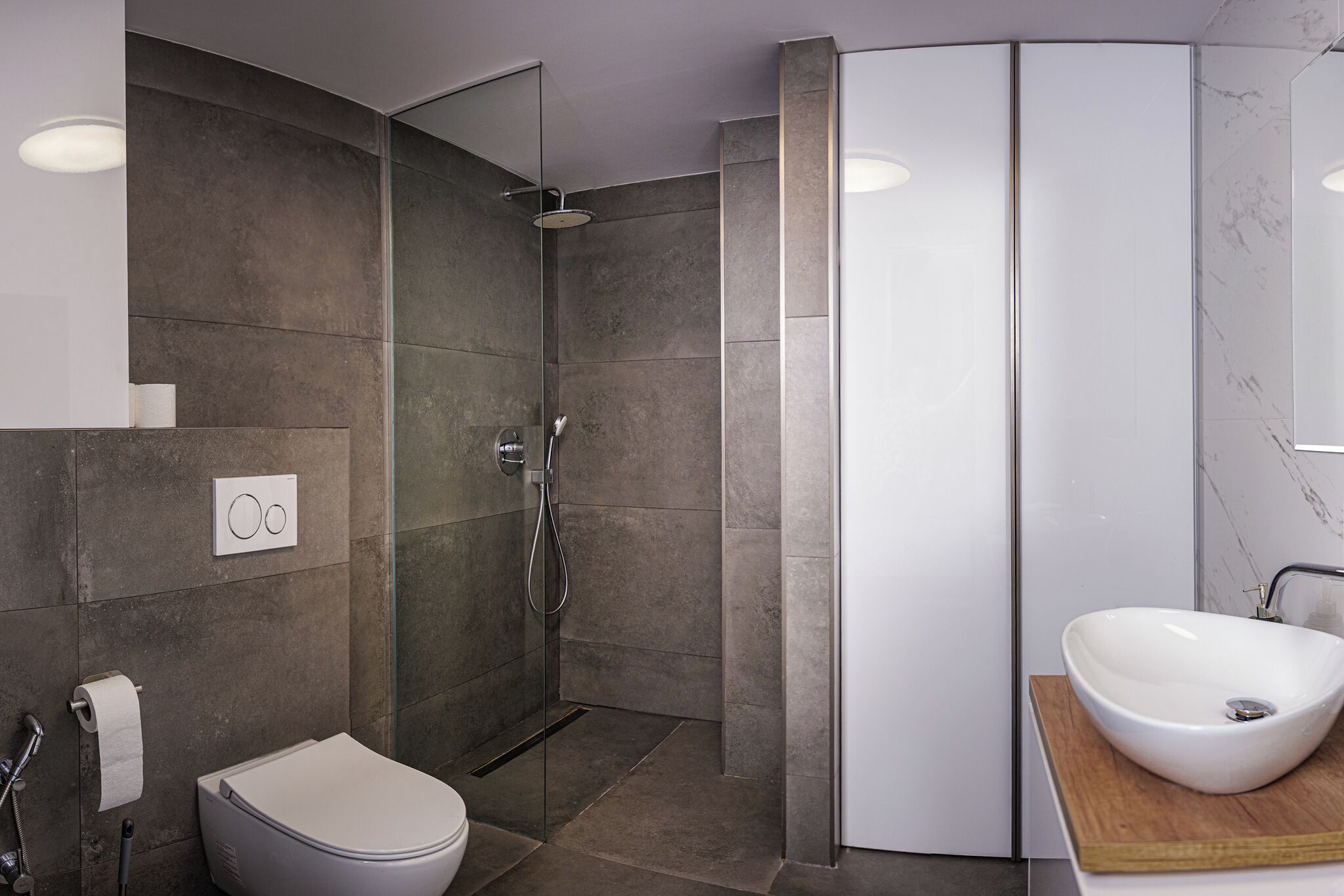Une salle de bain moderne avec une douche à parois de verre, des toilettes blanches et un grand lavabo sur un plan de travail en bois.