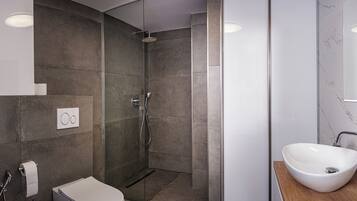 Une salle de bain moderne avec une douche à parois de verre, des toilettes blanches et un grand lavabo sur un plan de travail en bois.