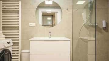 Een moderne badkamer met een ingebouwde wasmachine, een wastafel en een douche met glazen wanden.