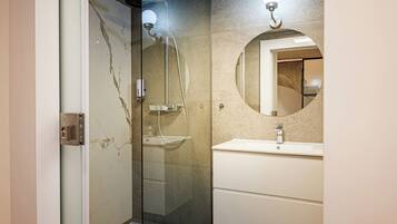 Een moderne badkamer met een douche met glazen wand, een ronde spiegel en een witte wastafel.