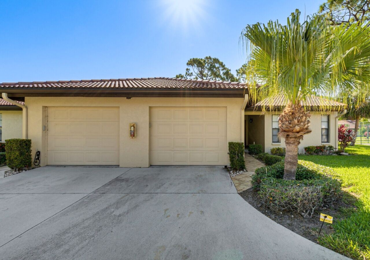 A two-story house with a garage, a driveway, and a well-maintained lawn with a palm tree.