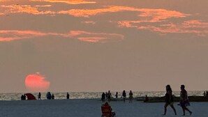 Ein Strandbild mit Menschen, die spazieren gehen, und einem Sonnenuntergang im Hintergrund.