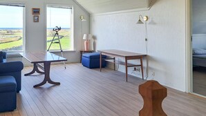 A room with a wooden floor, a table, a chair, a sofa, and a view of the outdoors through a window. - 3 bedroom stunning home in Vanse (Vanse)