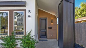 Ett modernt hus i två våningar med en mörk ytterdörr, en liten veranda och en välskött gräsmatta.