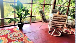 Ein Zimmer mit großen Fenstern, einem Blumentopf, einem Schaukelstuhl und einem gemusterten Teppich.