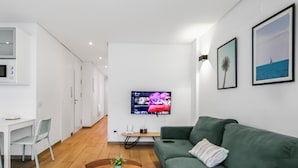 Een moderne woonkamer met een groene bank, een houten salontafel en een flatscreen televisie aan de muur.