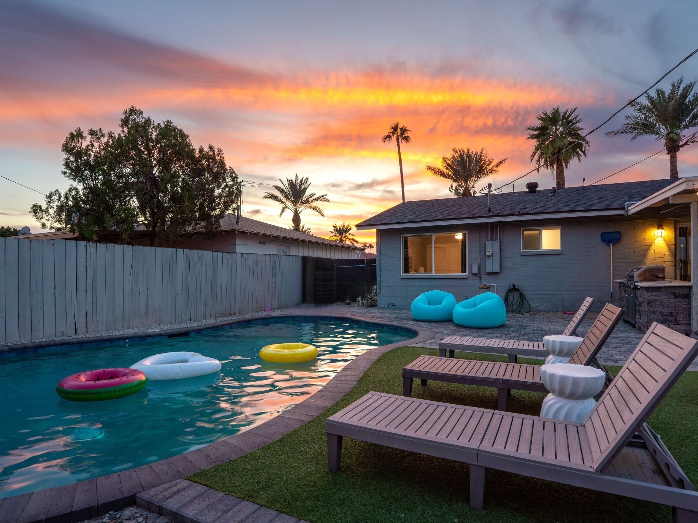 A backyard with a swimming pool, lounge chairs, and a house with a patio.