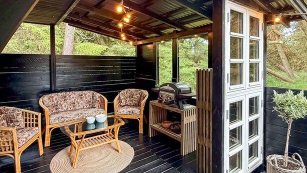 Un porche cubierto con muebles de mimbre, una parrilla y vistas a la vegetación.