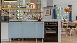 Una cocina con estufa antigua, un colgador para ollas y una ventana con vista a la vegetación.