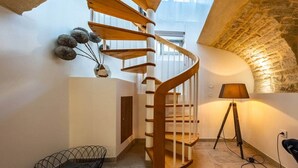 A spiral staircase in a room with a stone wall, a lamp, and a wire basket on the floor. - Le loft sur rivière (Dijon)