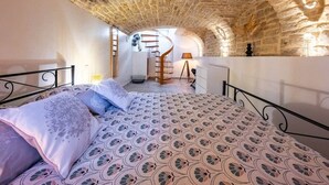 A bedroom with a patterned bedspread, a spiral staircase, and stone walls. - Le loft sur rivière (Dijon)