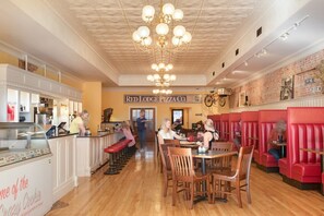 A restaurant interior with wooden flooring, red booths, and a central chandelier. - Gunslinger Gateway Red Lodge (Red Lodge)