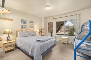 A bedroom with a large bed, a window with a view, a small table, and a lamp. - Gunslinger Gateway Red Lodge (Red Lodge)