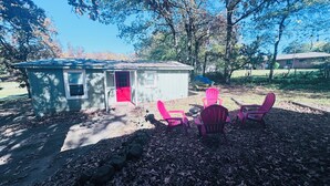Eine kleine Gartenhütte mit roter Tür, umgeben von einer Terrasse mit vier Adirondack-Stühlen.