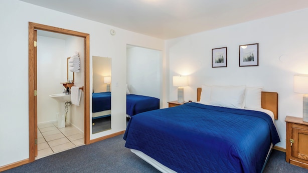 Une chambre d’hôtel avec un grand lit, deux tables de chevet, un miroir, un lavabo et deux tableaux encadrés accrochés au mur.