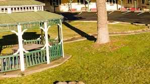 Un belvédère doté d’un toit vert et de bordures blanches, une pelouse délimitée par une bordure de pierres et un arbre en arrière-plan.