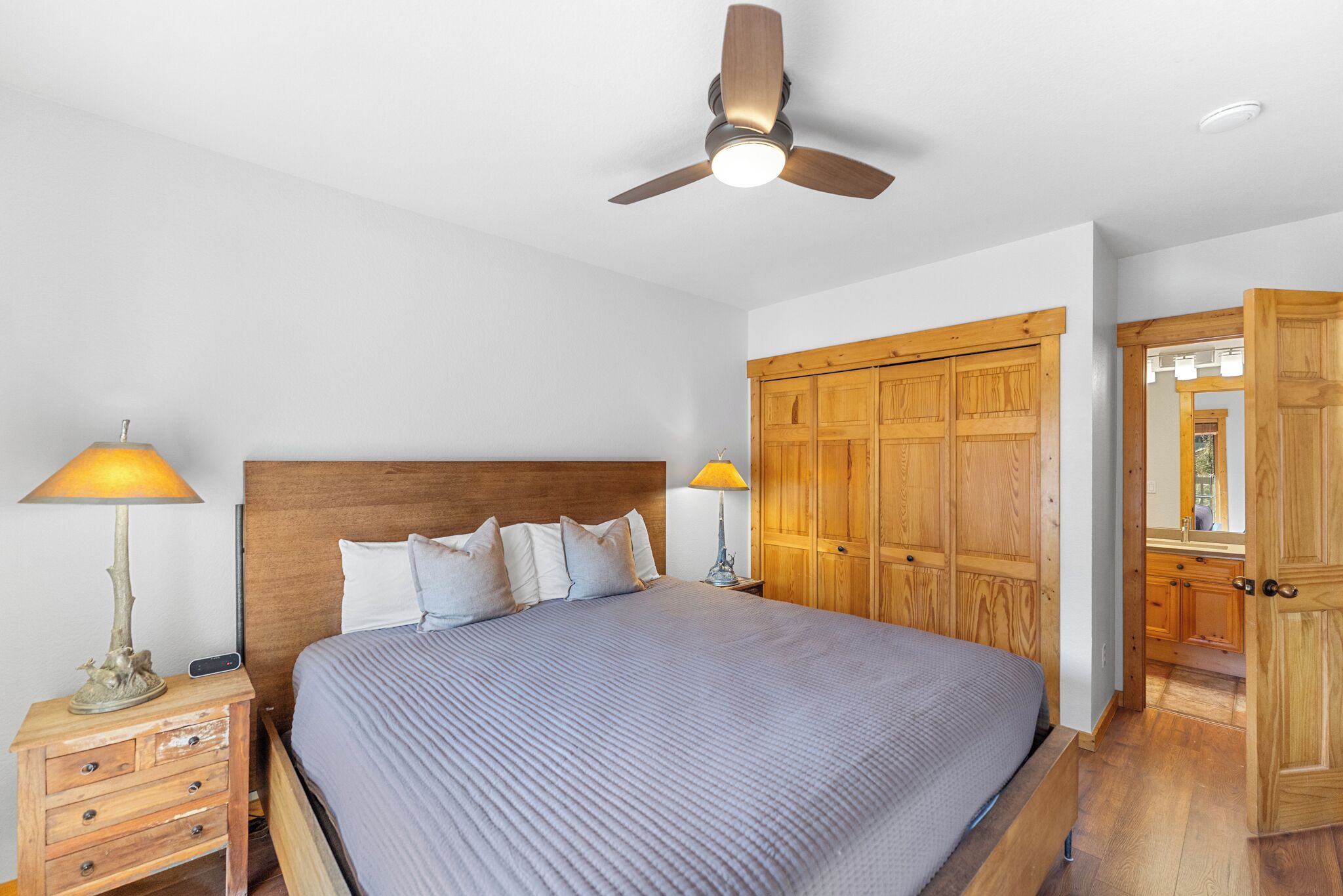 A bedroom with a bed, wooden wardrobe, nightstands, and a ceiling fan.