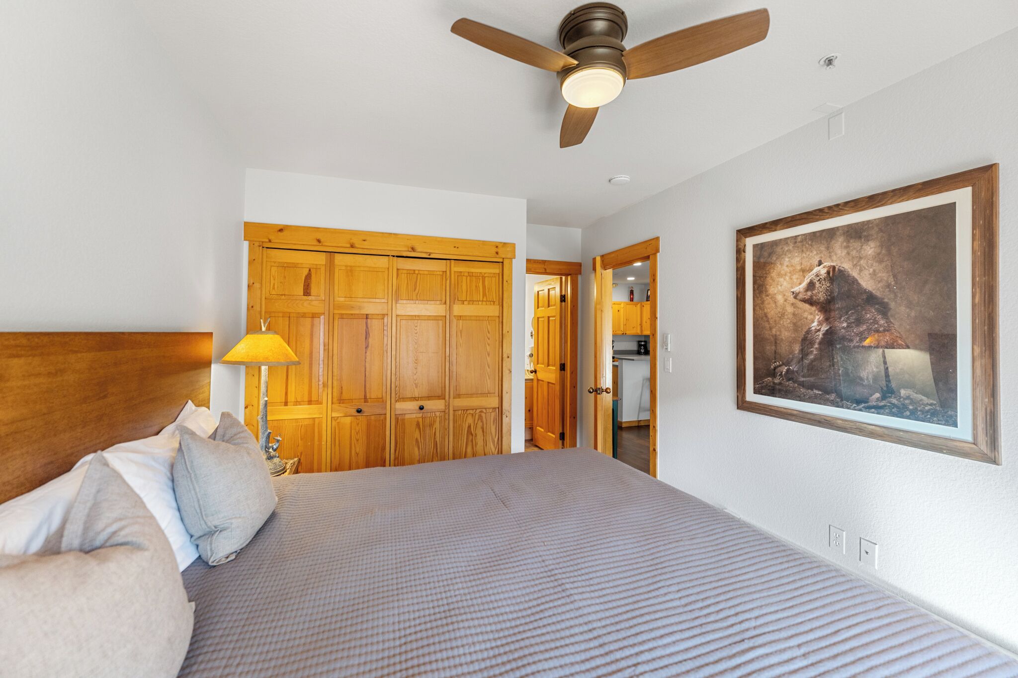 A bedroom with a large bed, wooden wardrobe, ceiling fan, and a framed painting on the wall.