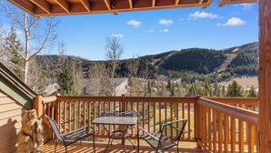 Une terrasse en bois avec une table et des chaises, offrant une vue sur un paysage montagneux.