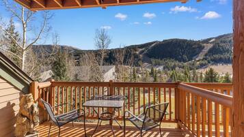 A wooden deck with a table and chairs, overlooking a mountainous landscape.