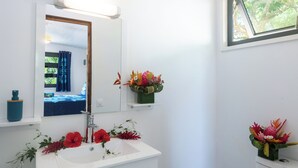 Een badkamer met een wit wastafel, spiegel en toilet. Er staan bloemstukken op de wastafel en boven het toilet bevindt zich een raam.