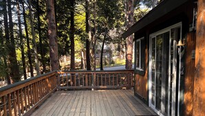 A wooden deck with a railing, surrounded by tall trees. - Beautiful 3-bedroom cabin in Lake Arrowhead perfect for relaxing getaways! (Lake Arrowhead)