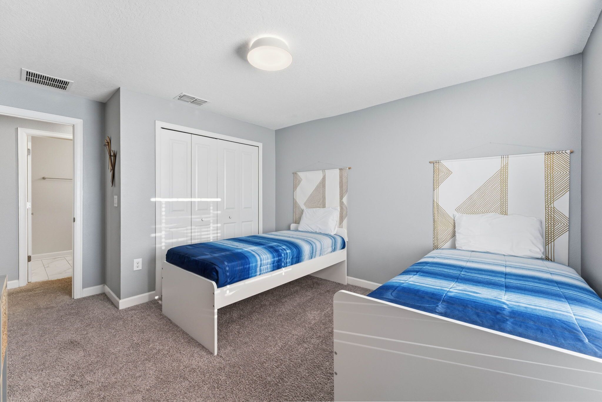 Une chambre avec deux lits simples, une armoire blanche et un luminaire au plafond.
