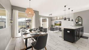 A modern kitchen and dining area with a large island, pendant lighting, and a view of the outdoors. - Relaxing 4BR Villa with Pool in Champions Gate (Four Corners)