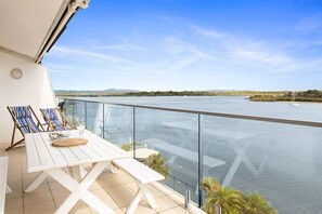 Ein Balkon mit Blick auf einen Fluss, einem Tisch mit Stühlen und blauem Himmel.