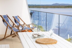 Ein Balkon mit zwei gestreiften Liegestühlen, einem Tisch mit Teller, Glas und einer gewebten Matte.