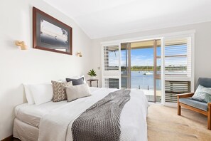 Ein Schlafzimmer mit Bett, einem Sessel, einer Pflanze und Blick auf das Wasser.